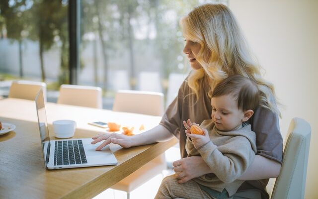 Frau arbeitet am Laptop mit Kleinkind im Arm