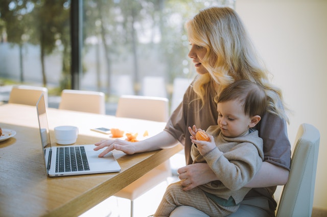 Frau arbeitet am Laptop mit Kleinkind im Arm